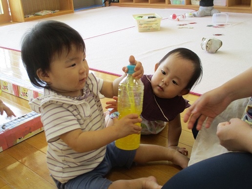 0才児が色水入りの容器を見ているところ